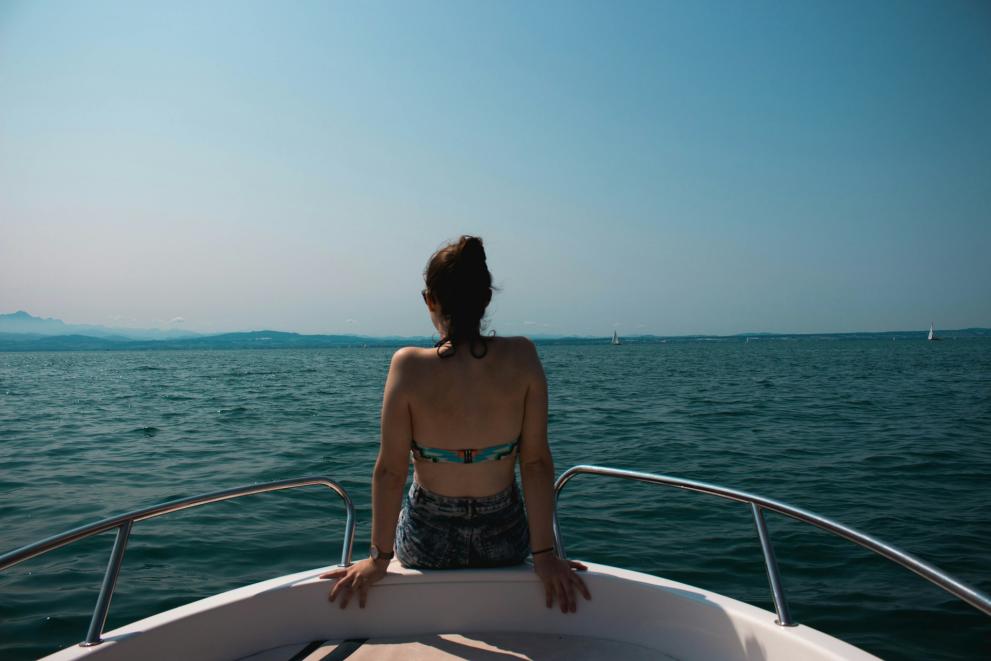 a woman is sitting on a small boat, she is facing a lake